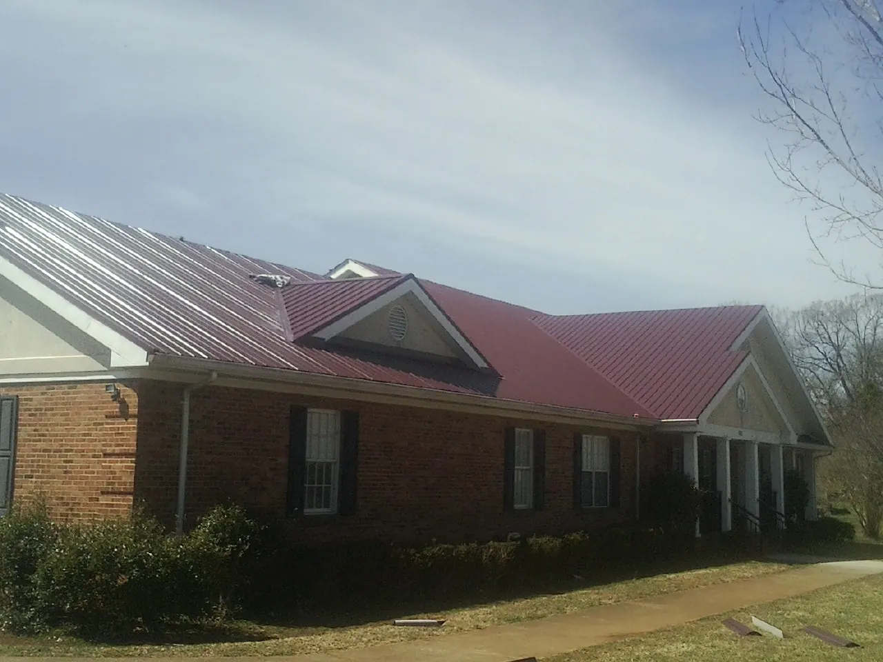 Red metal roof with gabled entries on a long brick building, from a Hail Damage Roof Repair job in Montrose